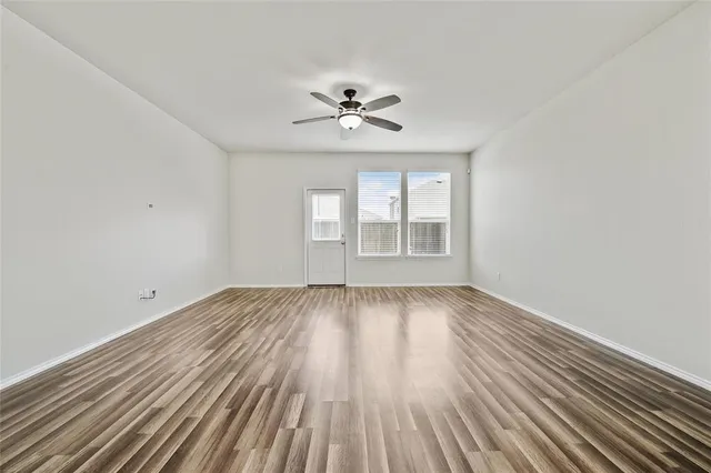 an empty room with wooden floor ceiling fan and windows