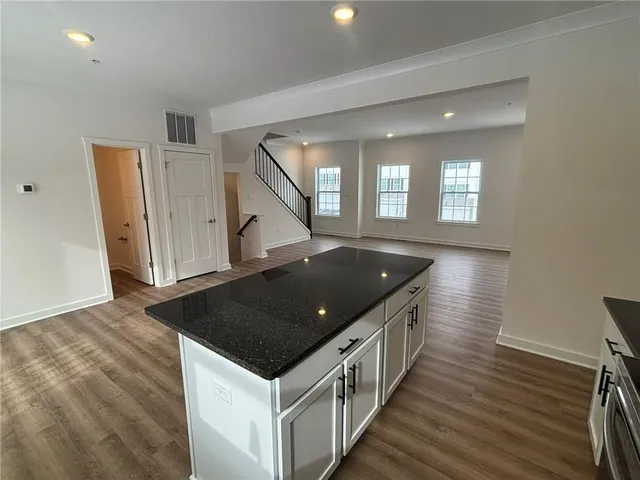 a kitchen with stainless steel appliances granite countertop a stove top oven a sink and white cabinets with wooden floor