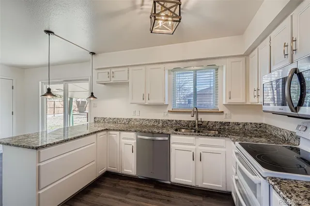 a kitchen with granite countertop a sink dishwasher a stove and white cabinets