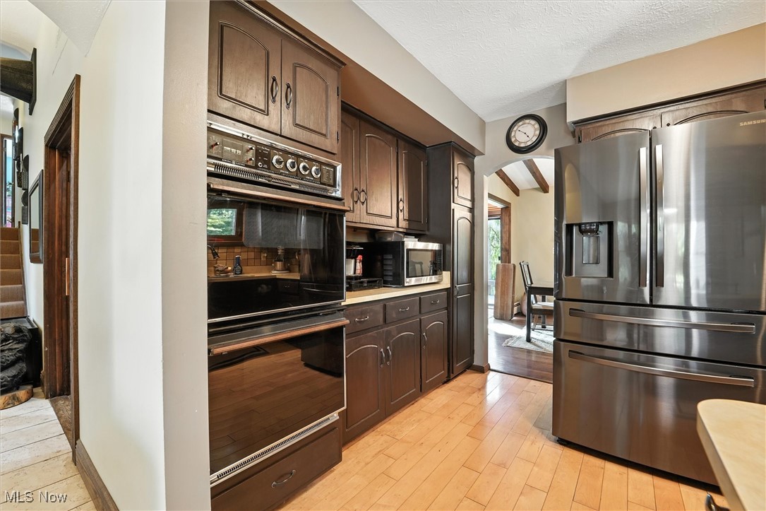12120 Caves Road Chesterland, OH 44026 - Photo 14 of 50 Kitchen with arched walkways, appliances with stainless steel finishes, dark brown cabinetry, light countertops, and light wood finished floors