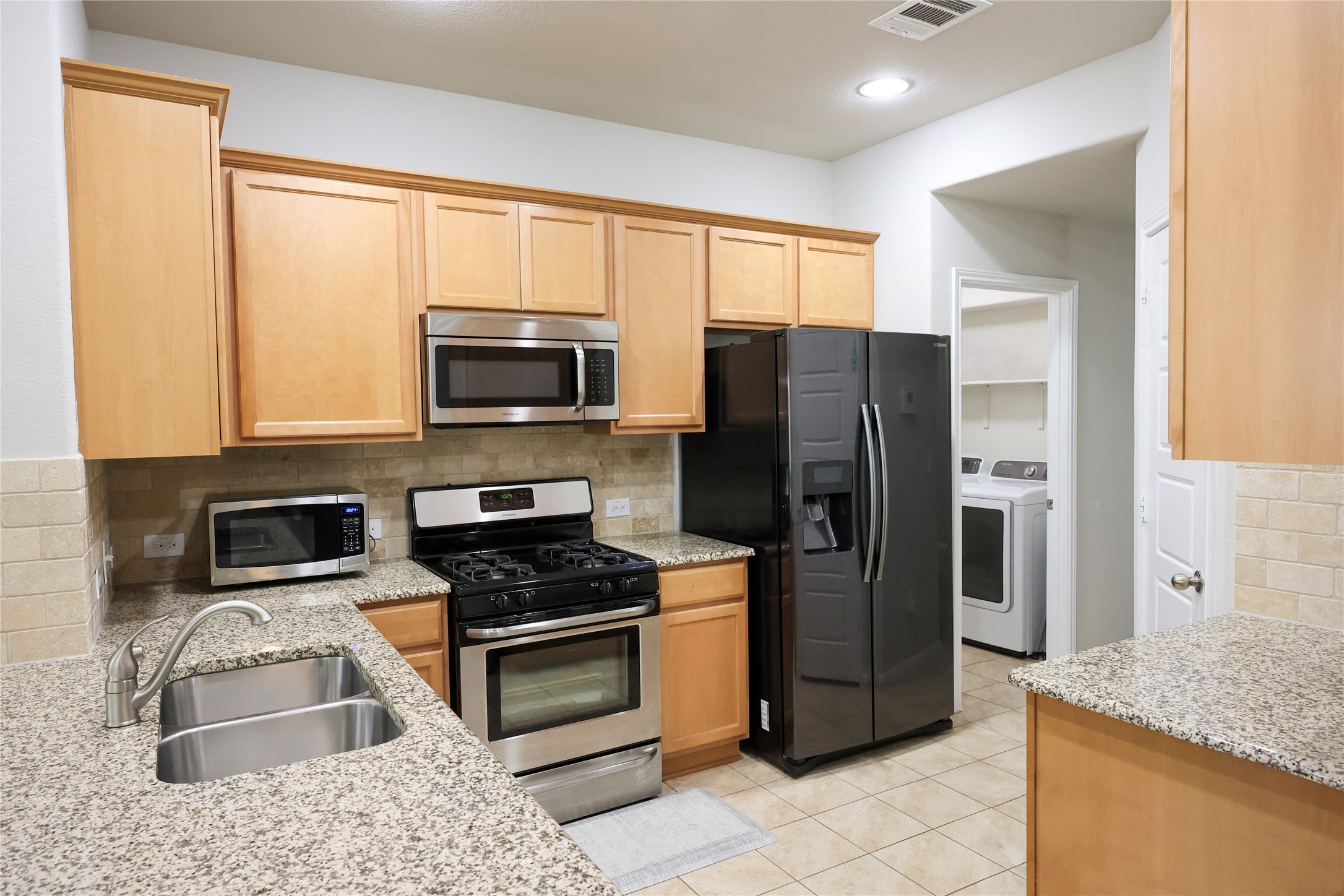 717 Schefer Street Leander, TX 78641 - Photo 7 of 27 a kitchen with granite countertop wooden cabinets a refrigerator and a stove top oven with granite countertops