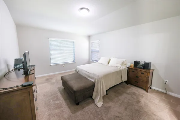 a spacious bedroom with a bed and a flat tv screen on dresser