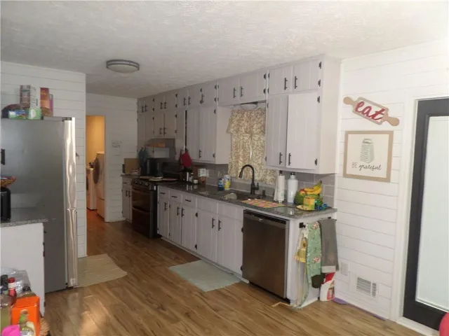 a kitchen with stainless steel appliances granite countertop a refrigerator a sink dishwasher and white cabinets with wooden floor