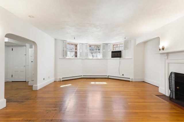 a view of an empty room with wooden floor and a fireplace