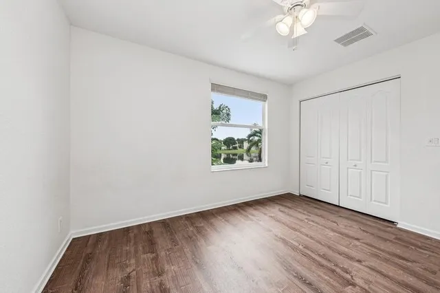 an empty room with wooden floor chandelier fan and windows