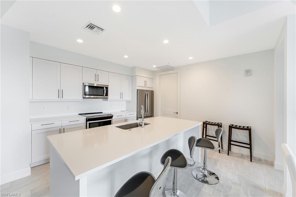 1111 Central, Unit 417S Naples, FL 34104 - Photo 11 of 25 a kitchen with stainless steel appliances a white stove top oven a sink a refrigerator with white cabinets and wooden floor