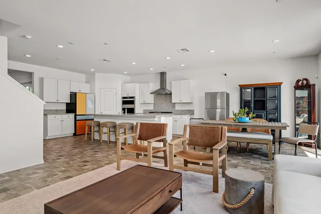 a living room with stainless steel appliances kitchen island granite countertop a dining table chairs and a refrigerator