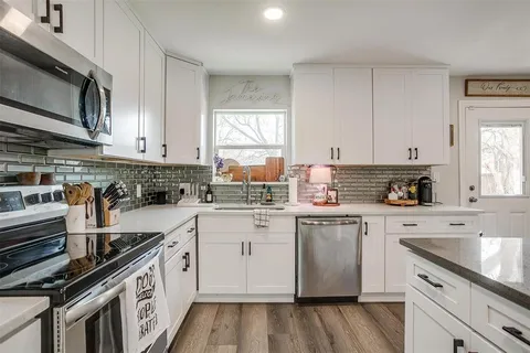 a kitchen with stainless steel appliances white cabinets sink and wooden floor