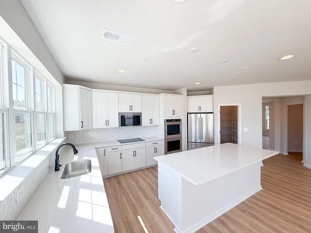 a large white kitchen with stainless steel appliances granite countertop a lot of counter space and wooden floors