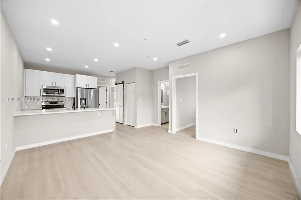 a view of kitchen with stainless steel appliances refrigerator oven and white cabinets with wooden floor