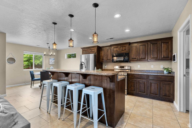 225 Falcon Court Ivins, UT 84738 - Photo 6 of 47 Kitchen featuring stainless steel appliances, dark wood finish cabinetry, a kitchen bar, light tile patterned flooring, and a textured ceiling