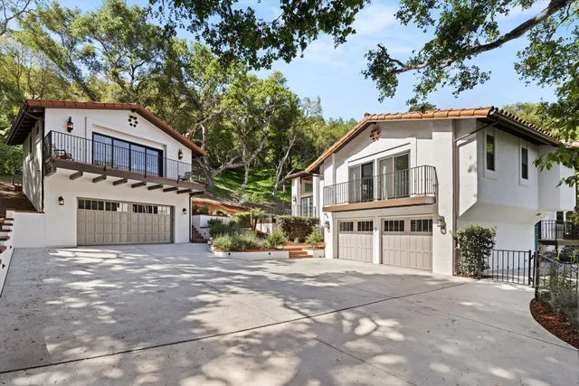 a view of a blue house with large trees and cars parked in front of it