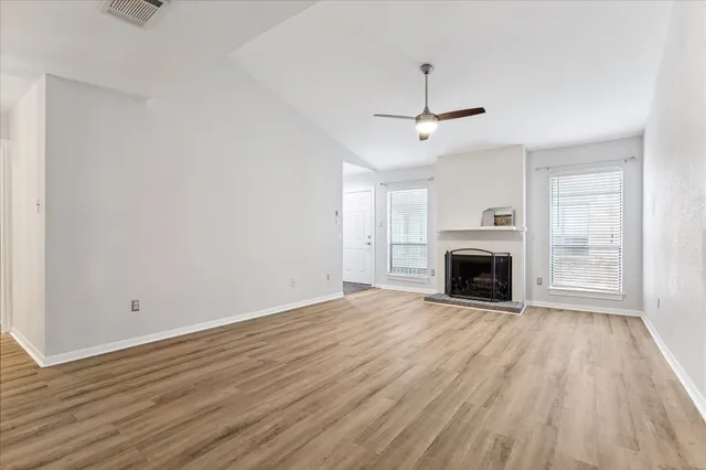an empty room with wooden floor fireplace and windows