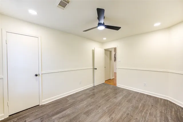 an empty room with wooden floor ceiling fan and refrigerator