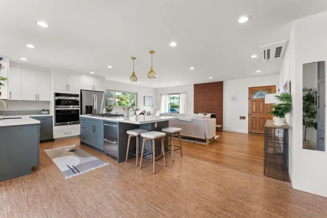 a open kitchen with stainless steel appliances kitchen island granite countertop a refrigerator a stove a sink a dining table and chairs with wooden floor