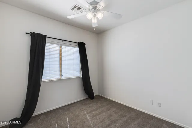 an empty room with chandelier fan and windows