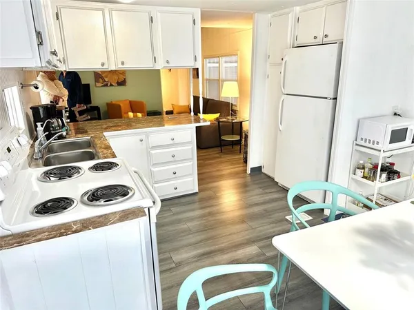 a view of a kitchen with kitchen island a stove a sink a refrigerator wooden floor and a dining table with wooden floor
