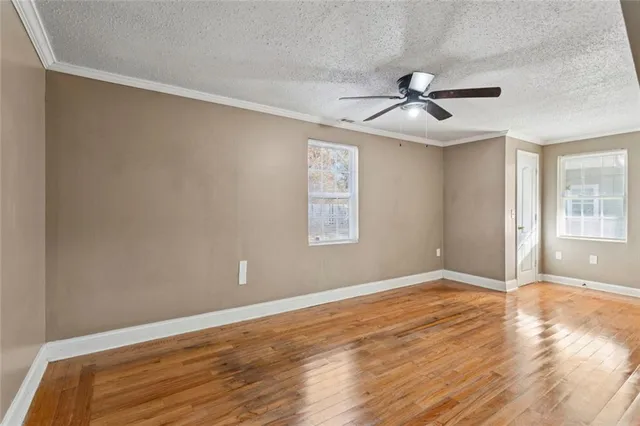 an empty room with wooden floor ceiling fan and windows