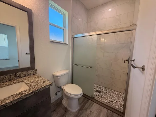 a bathroom with a granite countertop sink a toilet a shower and a mirror
