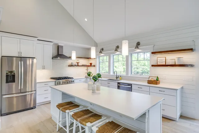 a kitchen with stainless steel appliances a stove a sink a refrigerator white cabinets and wooden floor