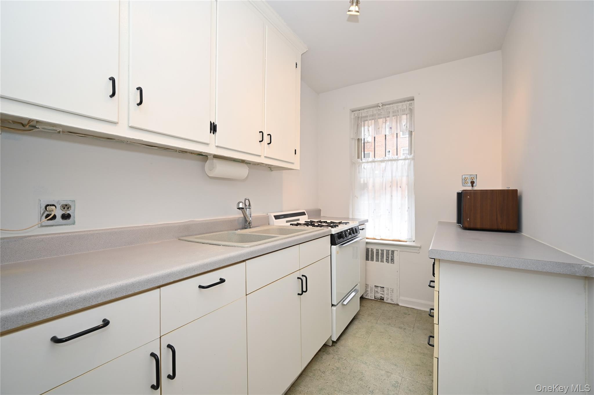 39-45 51st Street, Unit 1D Queens, NY 11377 - Photo 8 of 16 Kitchen featuring white cabinets, white range with gas stovetop, light countertops, and radiator