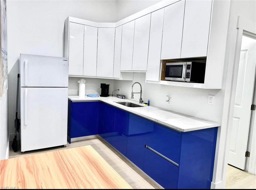 2881 Santa Barbara Boulevard Naples, FL 34116 - Photo 2 of 15 Kitchen featuring freestanding refrigerator, stainless steel microwave, a sink, white cabinets, and modern cabinets
