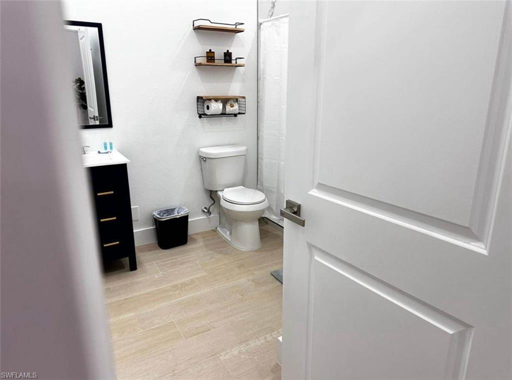 2881 Santa Barbara Boulevard Naples, FL 34116 - Photo 5 of 15 Bathroom with toilet, vanity, a shower with curtain, wood finished floors, and baseboards