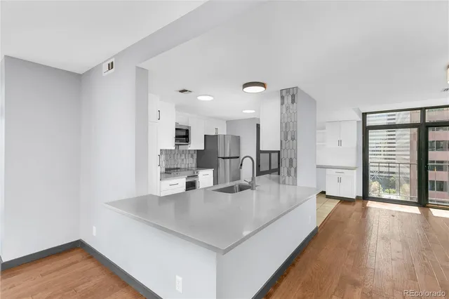 a living room with stainless steel appliances kitchen island granite countertop a refrigerator a sink a stove and white cabinets with wooden floor