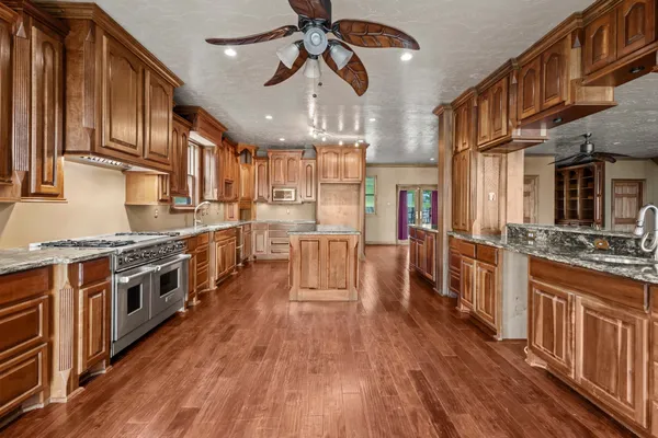 a large kitchen with stainless steel appliances granite countertop a stove top oven a refrigerator a dining table and chairs with wooden floor