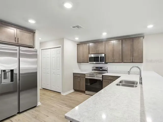 a kitchen with stainless steel appliances granite countertop a refrigerator a sink a stove top oven and a refrigerator with wooden floor