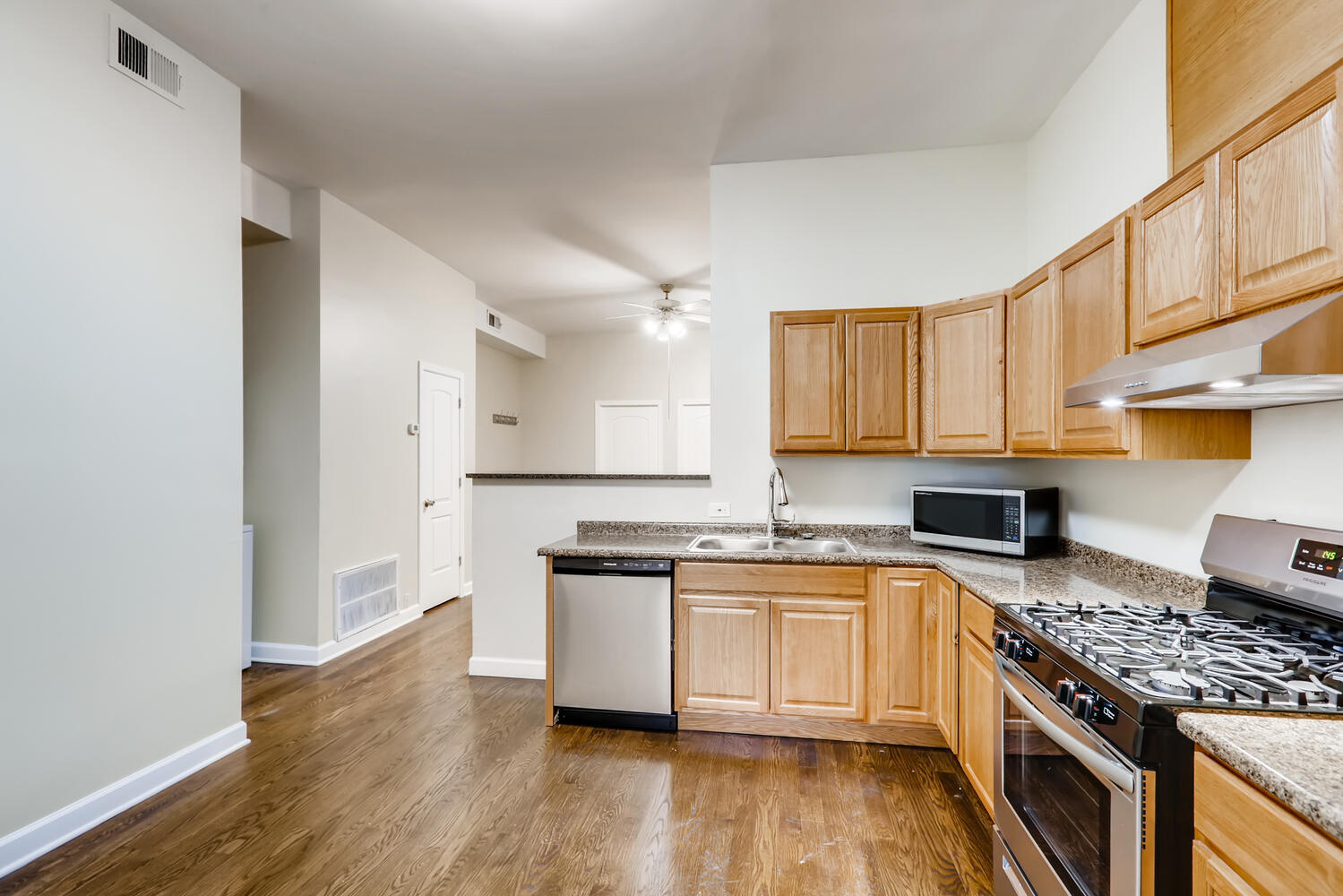 7046 North Clark Street, Unit 2 Chicago, IL 60626 - Photo 6 of 11 a kitchen with stainless steel appliances granite countertop a stove top oven a sink dishwasher and white cabinets with wooden floor