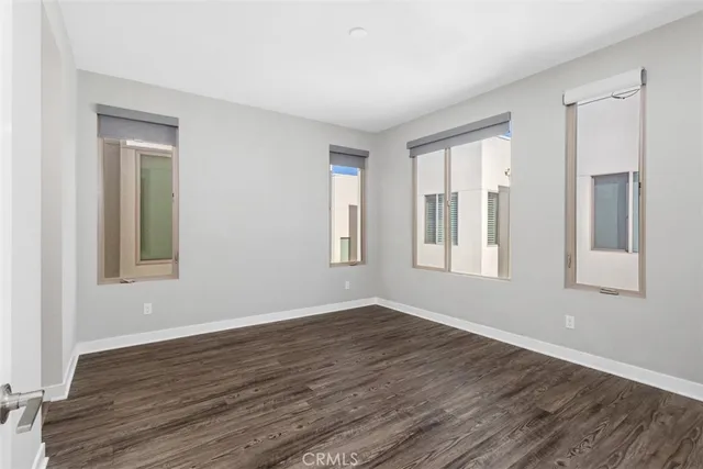 a view of an empty room with wooden floor and a kitchen