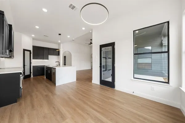 a view of kitchen with stainless steel appliances granite countertop a stove top oven a sink dishwasher a microwave oven and a dining table with wooden floor