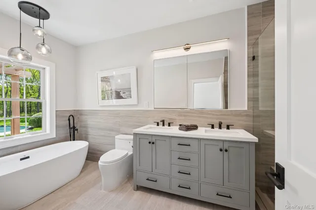 a bathroom with a double vanity sink a toilet a mirror and a bathtub