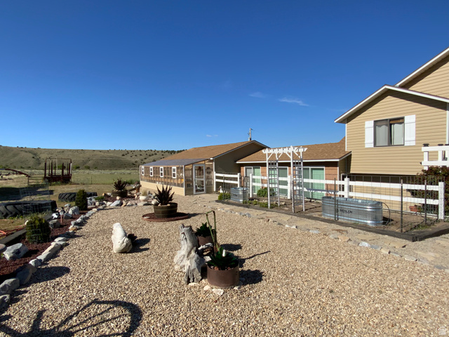 1061 Copper Street Stockton, UT 84071 - Photo 37 of 43 Expansive gravel landscaping featuring decorative rocks and planters, a multi-pane greenhouse, and a split-rail fence with wire mesh