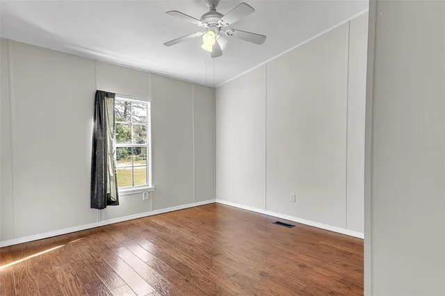 an empty room with wooden floor chandelier fan and windows