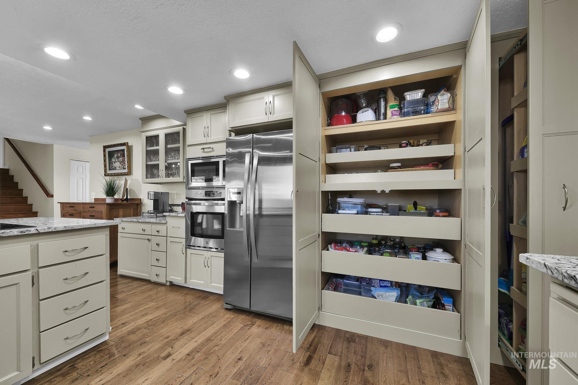 315 East Pat Lane Caldwell, ID 83607 - Photo 16 of 50 Kitchen featuring stainless steel appliances, light granite countertops, hardwood flooring, glass insert cabinets, and recessed lighting