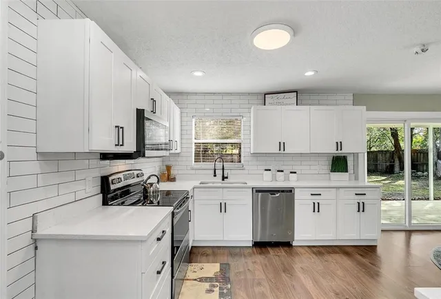 a kitchen with stainless steel appliances a sink a stove a refrigerator cabinets and a dining table with wooden floor