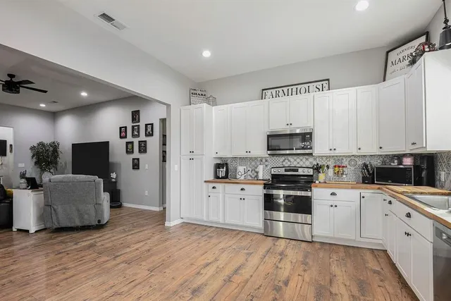 a kitchen with stainless steel appliances a stove top oven a sink a refrigerator white cabinets and wooden floor