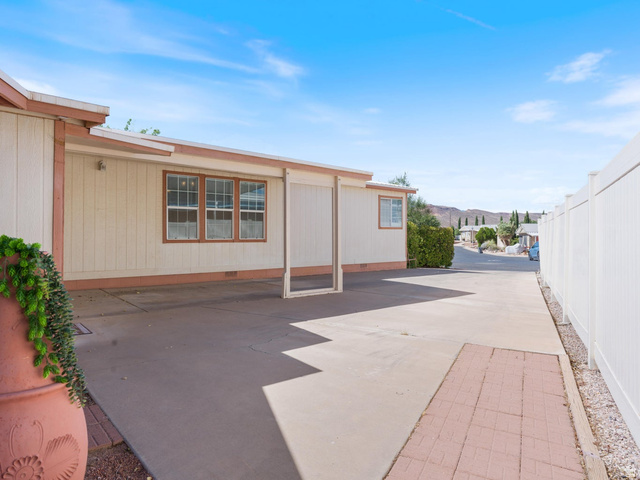 3941 West 40 North Hurricane, UT 84737 - Photo 7 of 55 Exterior features include a tan facade with brown trim, covered parking area, concrete paving, and a white privacy fence