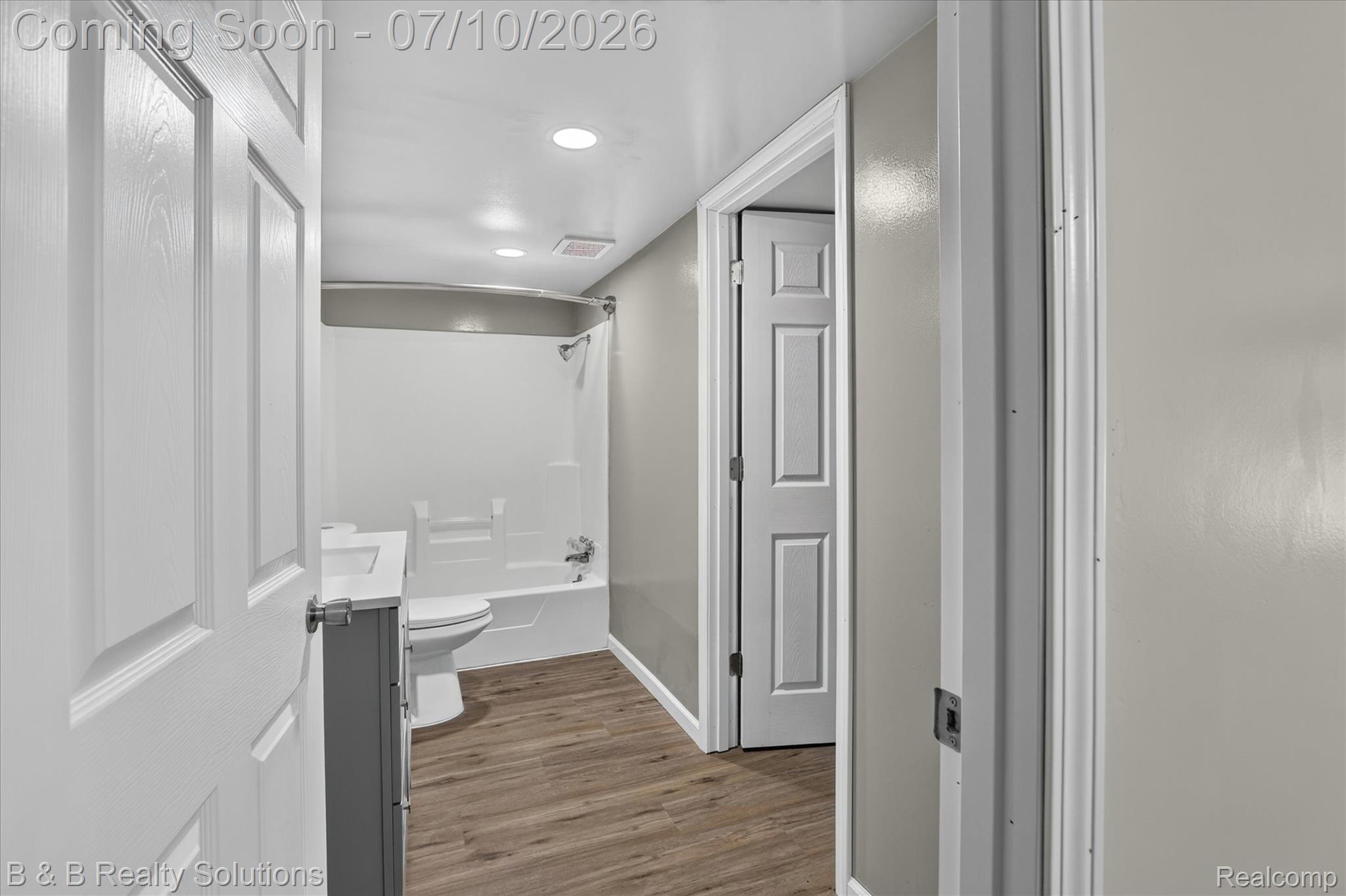 1564 East Burnside Road North Branch, MI 48461 - Photo 10 of 25 Bathroom featuring wood-finish flooring, a white vanity with an integrated sink, a commode, and a shower/tub combination with a curved shower rod