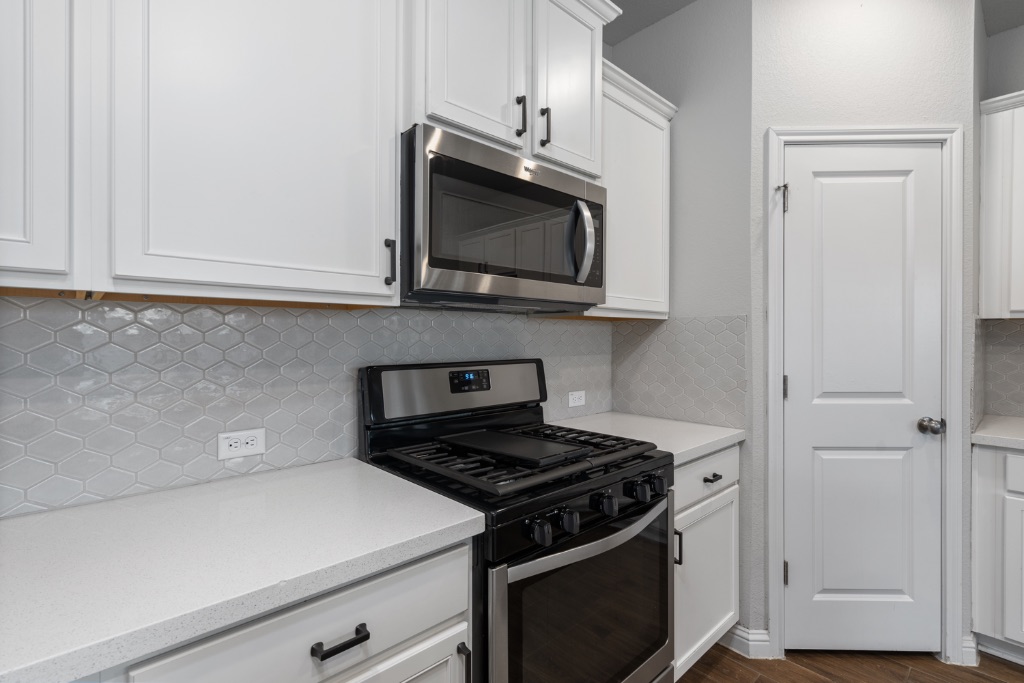 8301 Turnberry Lane Austin, TX 78744 - Photo 11 of 33 Kitchen featuring appliances with stainless steel finishes, backsplash, white cabinetry, light stone counters, and dark wood-style floors