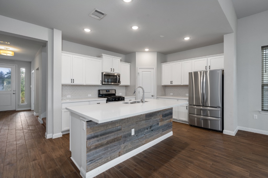 8301 Turnberry Lane Austin, TX 78744 - Photo 10 of 33 Kitchen featuring appliances with stainless steel finishes, white cabinets, a kitchen island with sink, dark wood finished floors, and recessed lighting