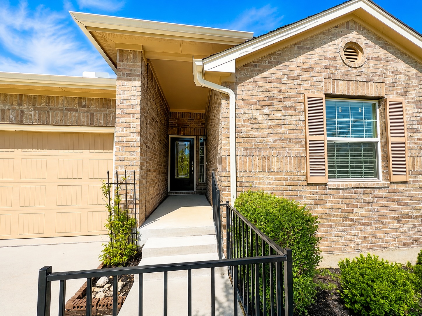 A welcoming brick entryway features concrete steps, black railings, and classic shutters.