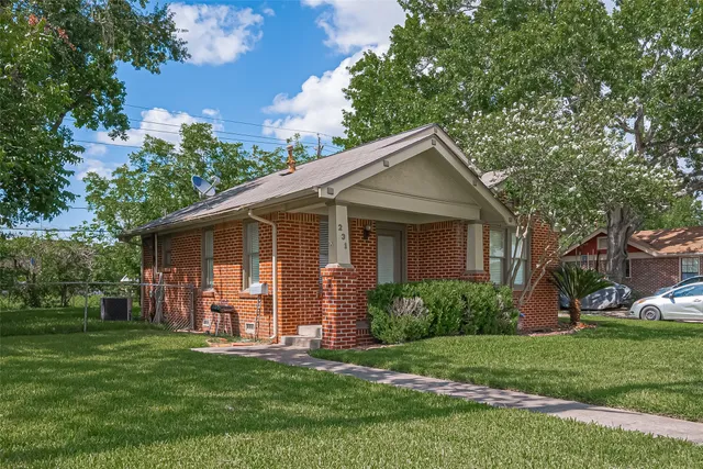 a view of a yard in front of a house with plants and large tree