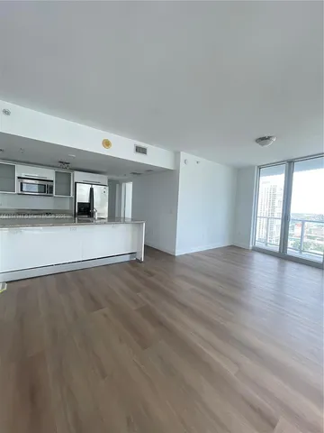 a view of an empty room with wooden floor and fan