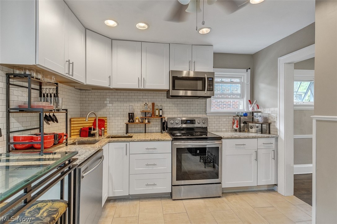 2972 Yorkshire Road Cleveland Heights, OH 44118 - Photo 12 of 44 Modern kitchen featuring white shaker cabinetry, stainless steel appliances, light-toned granite countertops, a subway tile backsplash, and ceramic tile flooring