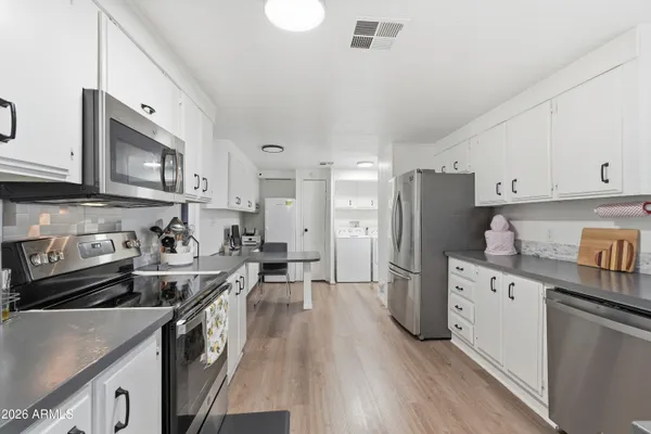 a kitchen with stainless steel appliances granite countertop a refrigerator a stove a sink dishwasher and white cabinets with wooden floor