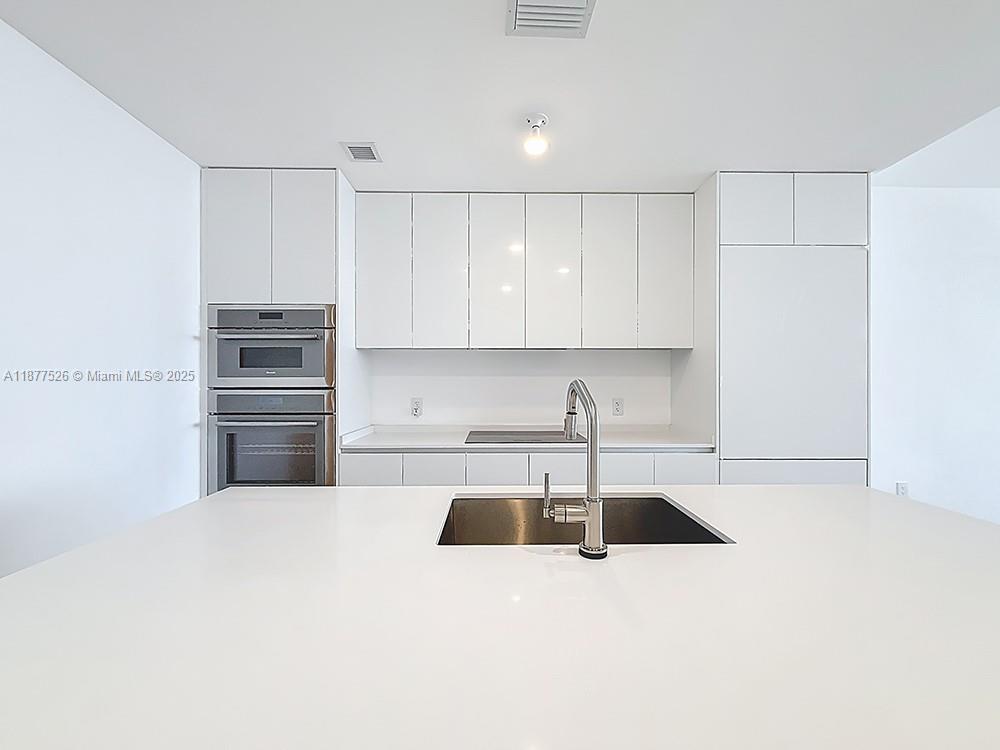 700 Northeast 24th Street, Unit 1402 Miami, FL 33137 - Photo 7 of 68 a kitchen with a sink stainless steel appliances and white cabinets