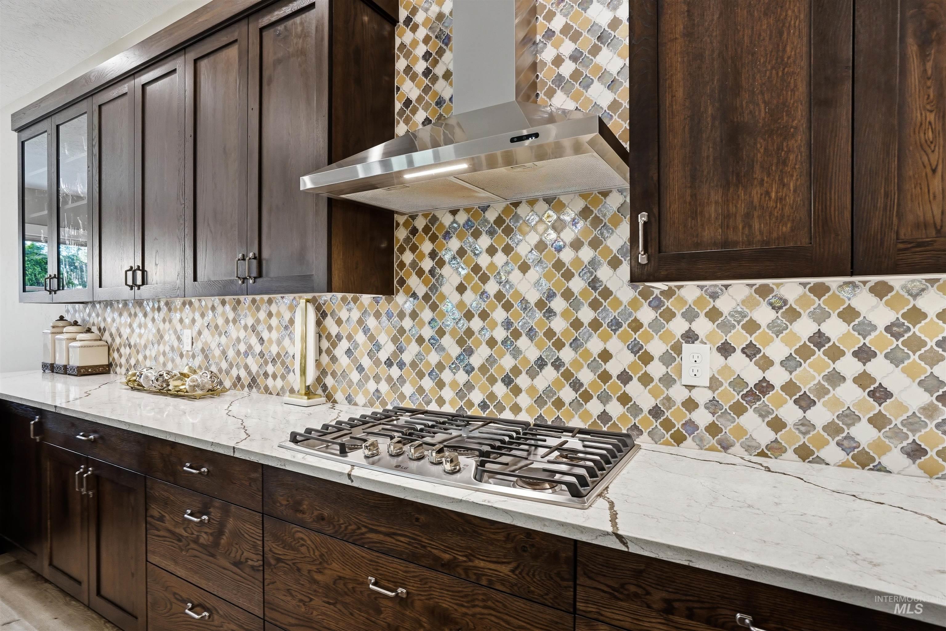 24165 Boer Goat Avenue Caldwell, ID 83607 - Photo 11 of 34 Kitchen featuring dark wood cabinetry, white countertops, a mosaic tile backsplash, a stainless steel gas range, and a coordinating stainless steel range hood